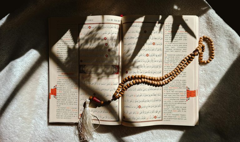 An open Quran with prayer beads resting on a sunlit cloth, creating a serene atmosphere.