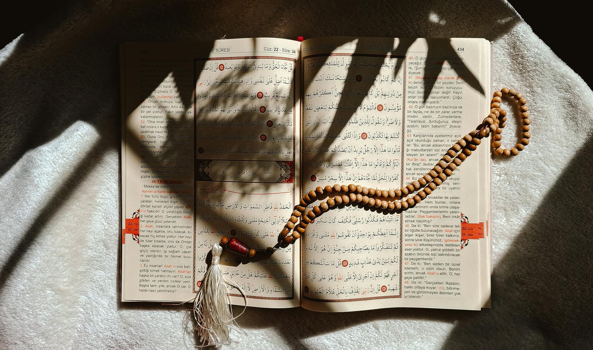 An open Quran with prayer beads resting on a sunlit cloth, creating a serene atmosphere.